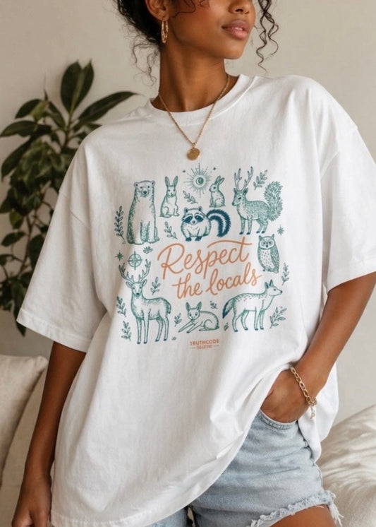 Person wearing a white t-shirt with animal graphics and text, standing indoors. Text says 'respect the locals' and design shows cute animals such as bunny, owl, deer, raccoon and bear.