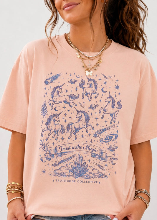 Person wearing a pink t-shirt with unicorn and star design, 'Trust in the Magic' text, and 'Truthcode Collective' branding.
