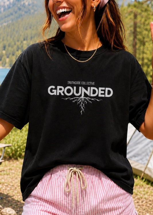 Person wearing a black t-shirt with 'GROUNDED' text and roots graphic, outdoors.