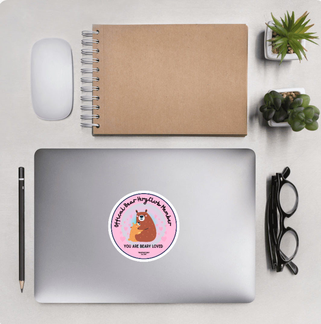 Aerial view of a desktop with laptop showing a circular sticker with bears hugging and text 'Official bear hug club member' and 'You are beary loved'