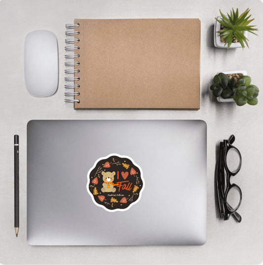 Aerial view of a desktop with laptop showing a scalloped circular sticker with a bear and autumn graphic design and text 'I love fall'