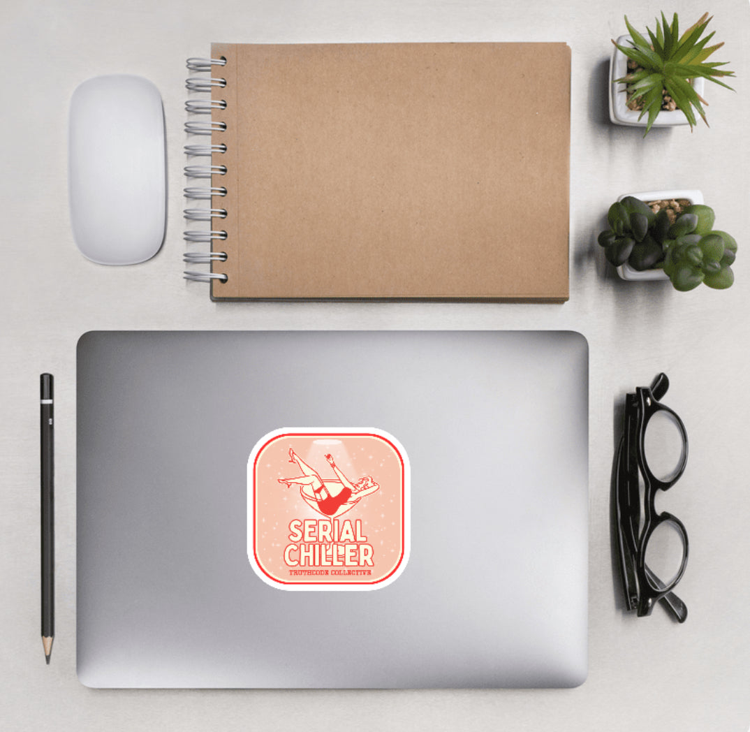 Aerial view of a desktop with laptop showing a squared sticker with a woman lying in a martini glass and text 'Serial Chiller'