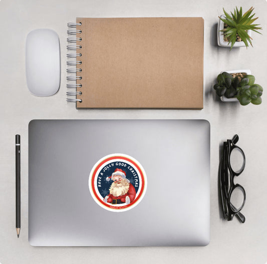 Laptop with a Santa Claus sticker and text 'Have a jolly good Christmas' and other desktop accessories around