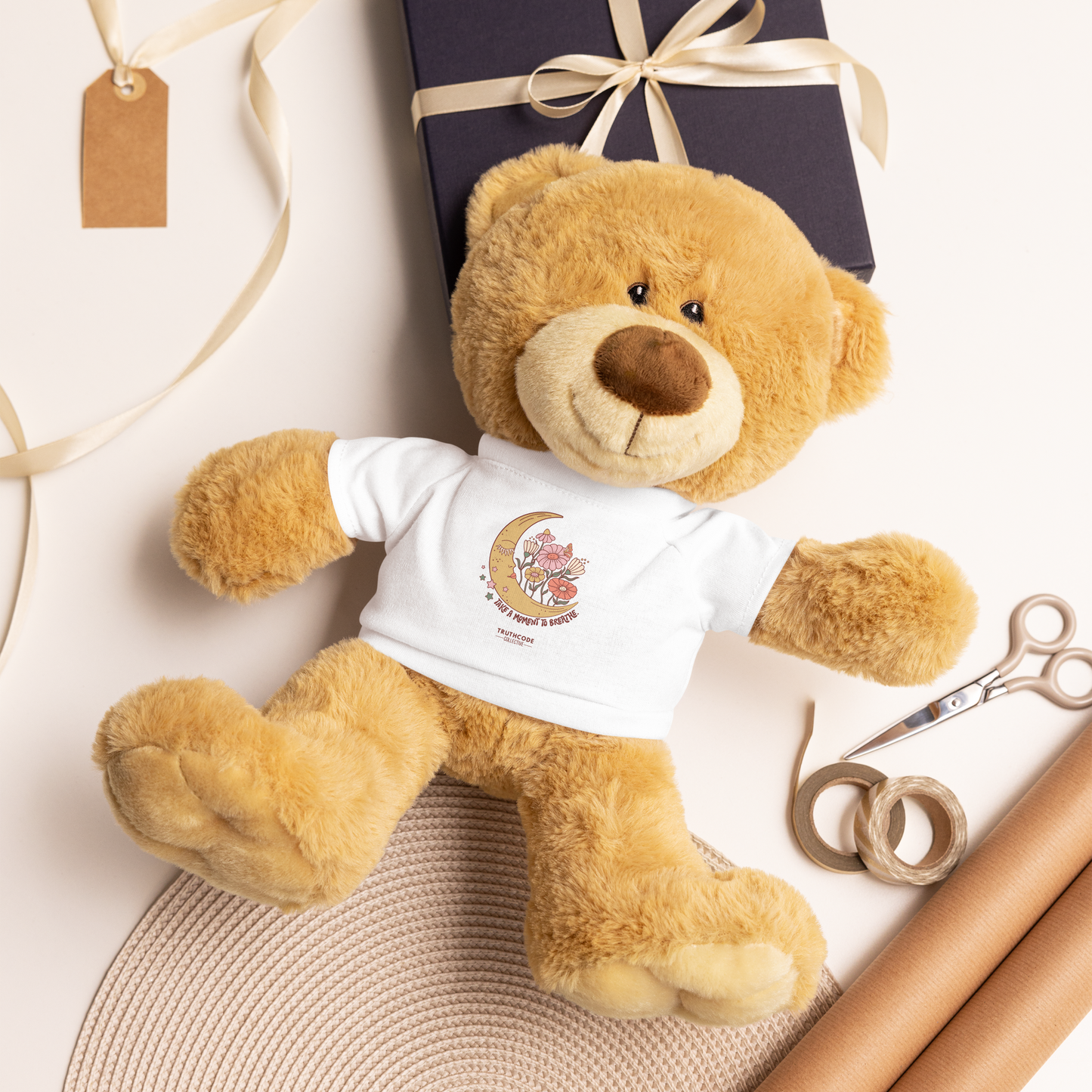 Plush teddy bear wearing a white t-shirt with a moon and floral design with a gift wrapping background
