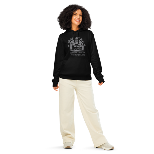 Woman wearing black organic hoodie with surf style graphic design and text 'Seas the day' on a white background