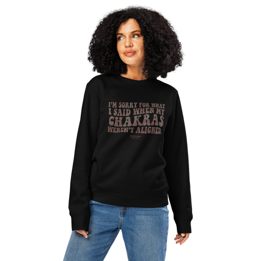 Woman wearing black organic sweatshirt with humorous text design 'I'm sorry for what I said when my chakras weren't aligned' on a white background