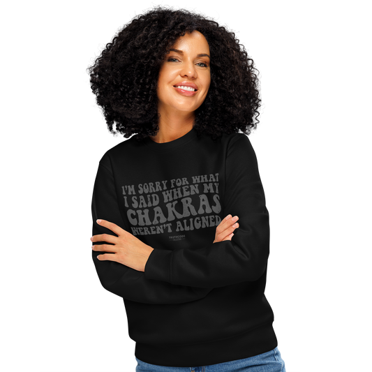 Woman wearing black organic sweatshirt with humorous text design 'I'm sorry for what I said when my chakras weren't aligned' on a white background