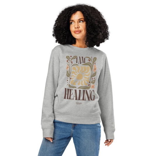 Woman wearing gray organic sweatshirt with 'I AM HEALING' text and floral design on a white background