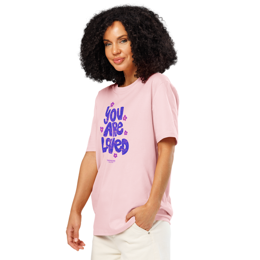 Woman wearing pink organic t-shirt with 'YOU ARE LOVED' text and daisy graphics, on a white background