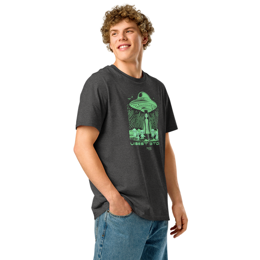 Guy wearing dark gray organic t-shirt with green alien abduction graphic and text 'Vibiest visitors' on a white background