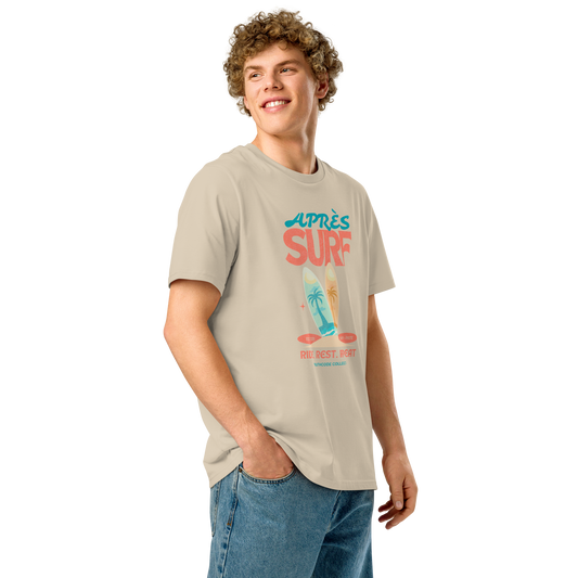 Person wearing a beige organic t-shirt with a surfing graphic design and text 'Après surf' on a white background