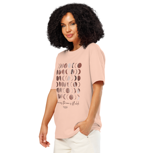 Woman wearing peach organic t-shirt with rose gold moon phase design and text 'Even in pieces, the moon is still whole', shirt on a white background