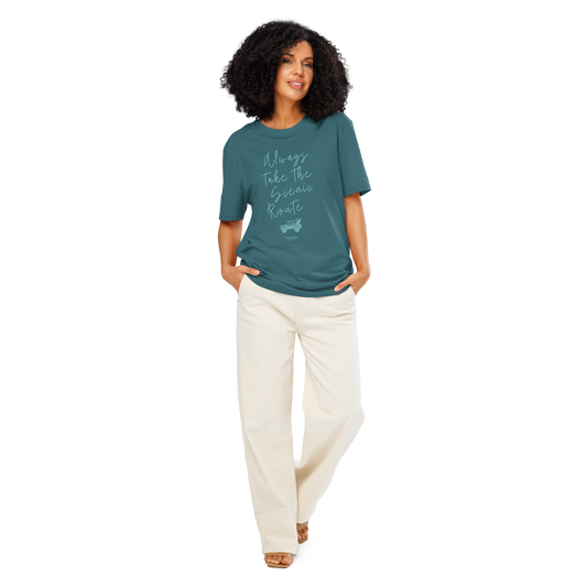 Woman wearing teal organic t-shirt with text design 'Always take the scenic route' with truck with surf board graphic on a white background