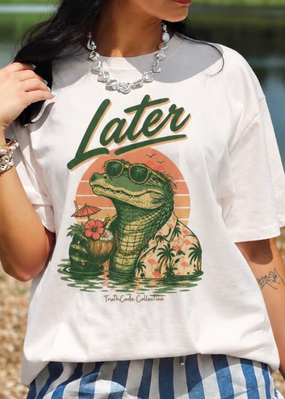 Person wearing a cute, humorous white t-shirt with a graphic design of a gator holding a tropical drink and 'Later' text.