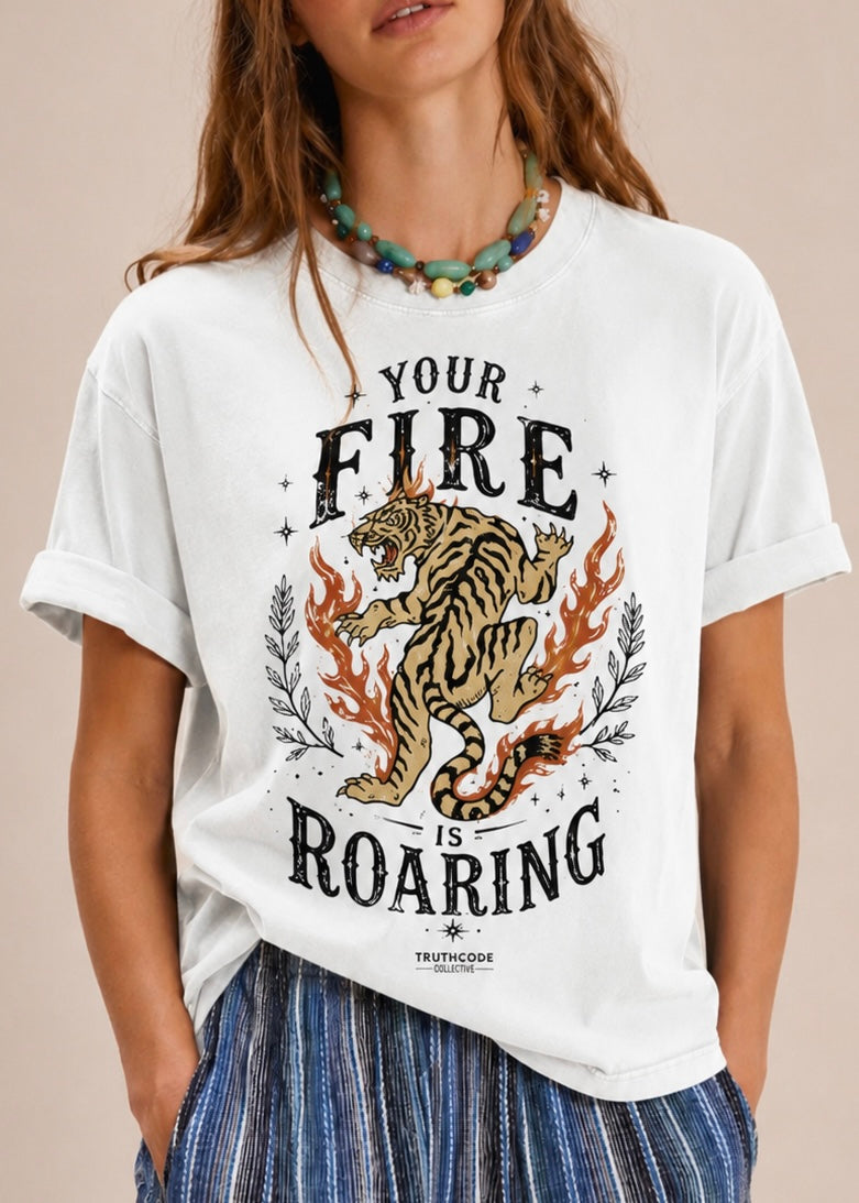 Person wearing a white t-shirt with a tiger graphic and text 'Your Fire is Roaring' on a beige background
