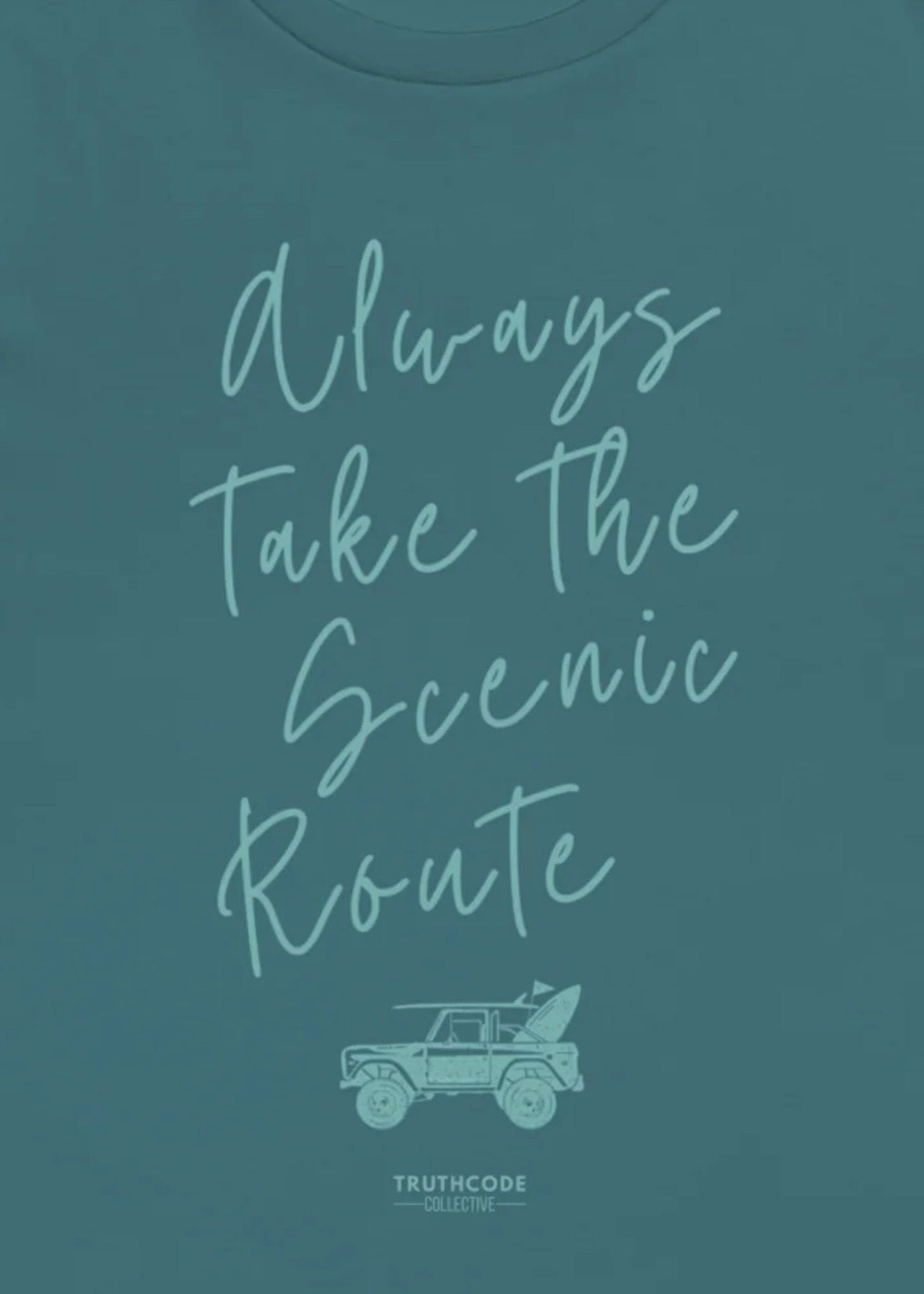 Close view of teal t-shirt with 'Always Take the Scenic Route' text and car graphic on a teal background