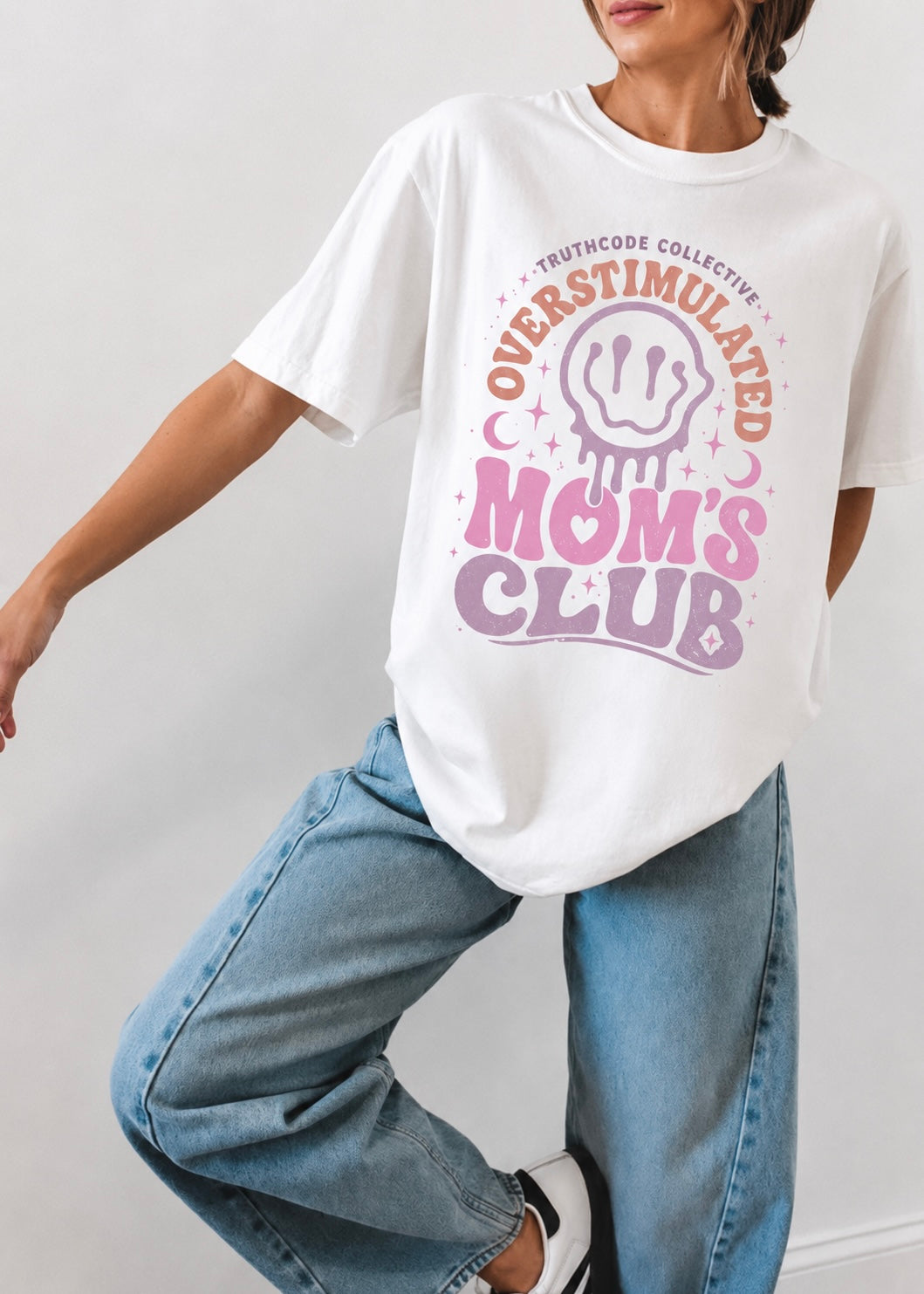 Person wearing a white t-shirt with 'Overstimulated Mom's Club' text and graphic on a plain background