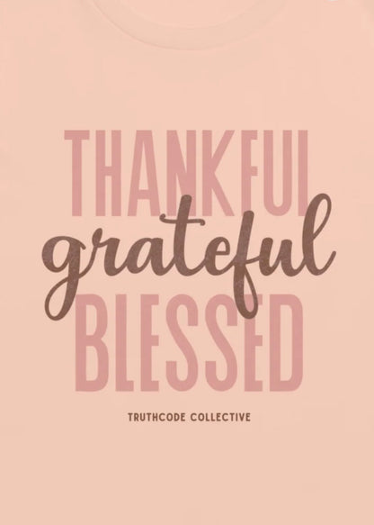 Peach t-shirt with motivational quote 'Thankful, grateful, blessed' and 'Truthcode Collective' branding.