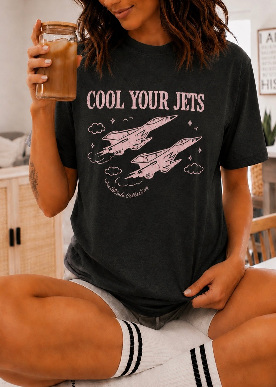 Person wearing a black t-shirt with 'Cool Your Jets' graphic design, holding a drink.