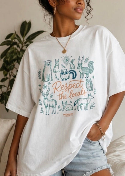 Person wearing a white t-shirt with animal graphics and text, standing indoors. Text says 'respect the locals' and design shows cute animals such as bunny, owl, deer, raccoon and bear.