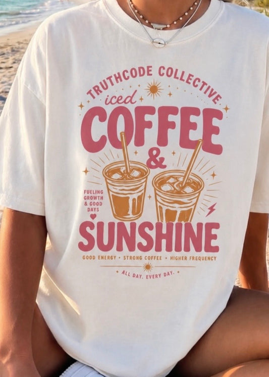 Person wearing a white t-shirt with 'Truthcode Collective iced coffee & sunshine' design at the beach.