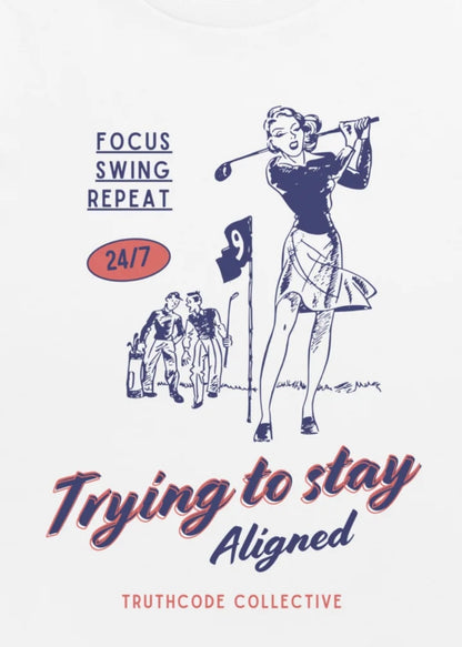 Close view of white t-shirt with vintage-style illustration of a woman playing golf with text 'Trying to stay aligned' and 'Truthcode Collective' 