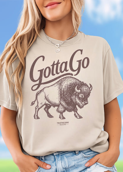 Person wearing a beige t-shirt with a graphic of a bison and 'Gotta Go' text, standing against a blue sky background.