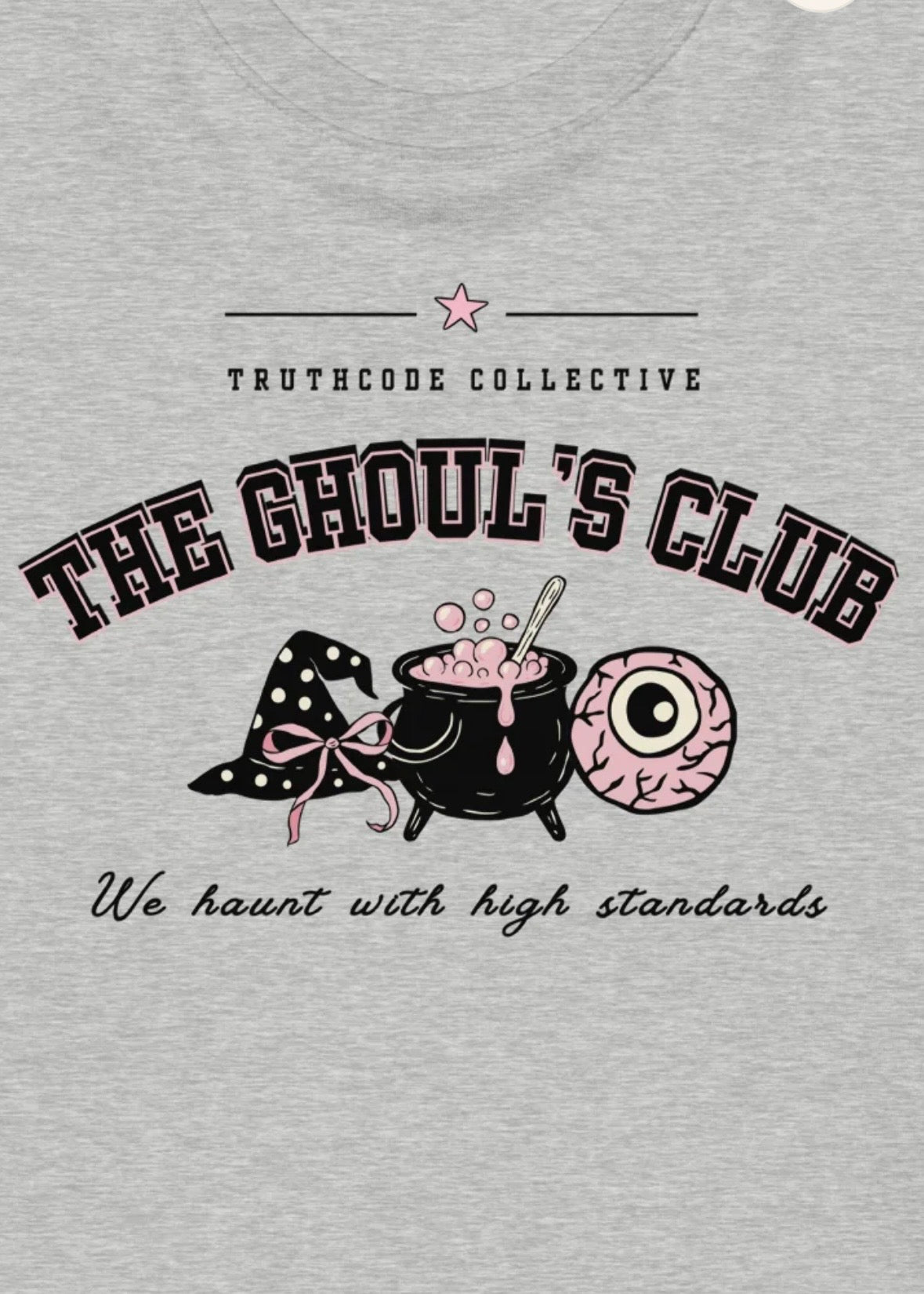 Close view of gray organic t-shirt with 'The Ghoul's Club, wea haunt you with high standards' graphic design featuring a witch hat, cauldron, and eye.
