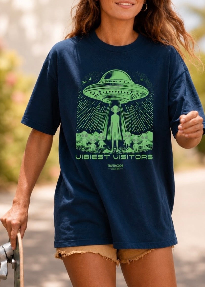 Person wearing a navy blue t-shirt with a green alien abduction graphic and text 'vibiest visitors'.