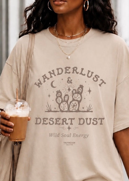 Person wearing a beige t-shirt with 'Wanderlust & Desert Dust' text and holding a drink.