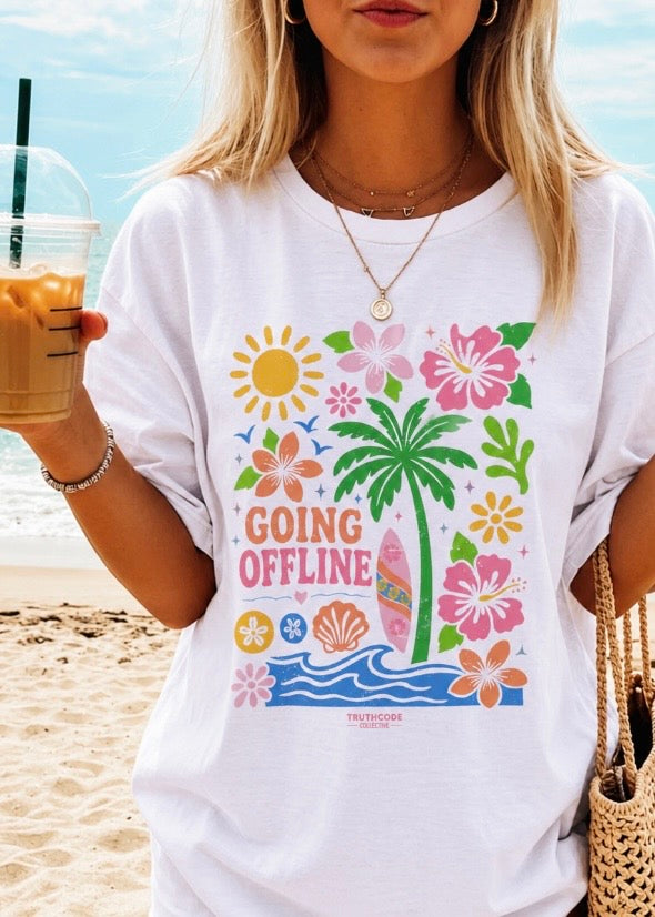 Person wearing a white t-shirt with a tropical design and 'Going Offline' text on a beach.