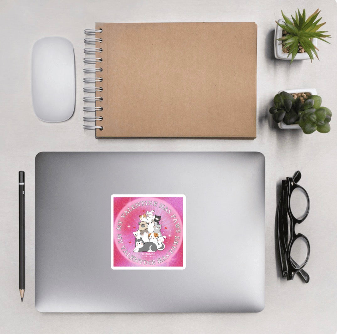 Sticker on a laptop with cartoon pets and 'My Valentine has paws' text on a pink background with desktop accessories