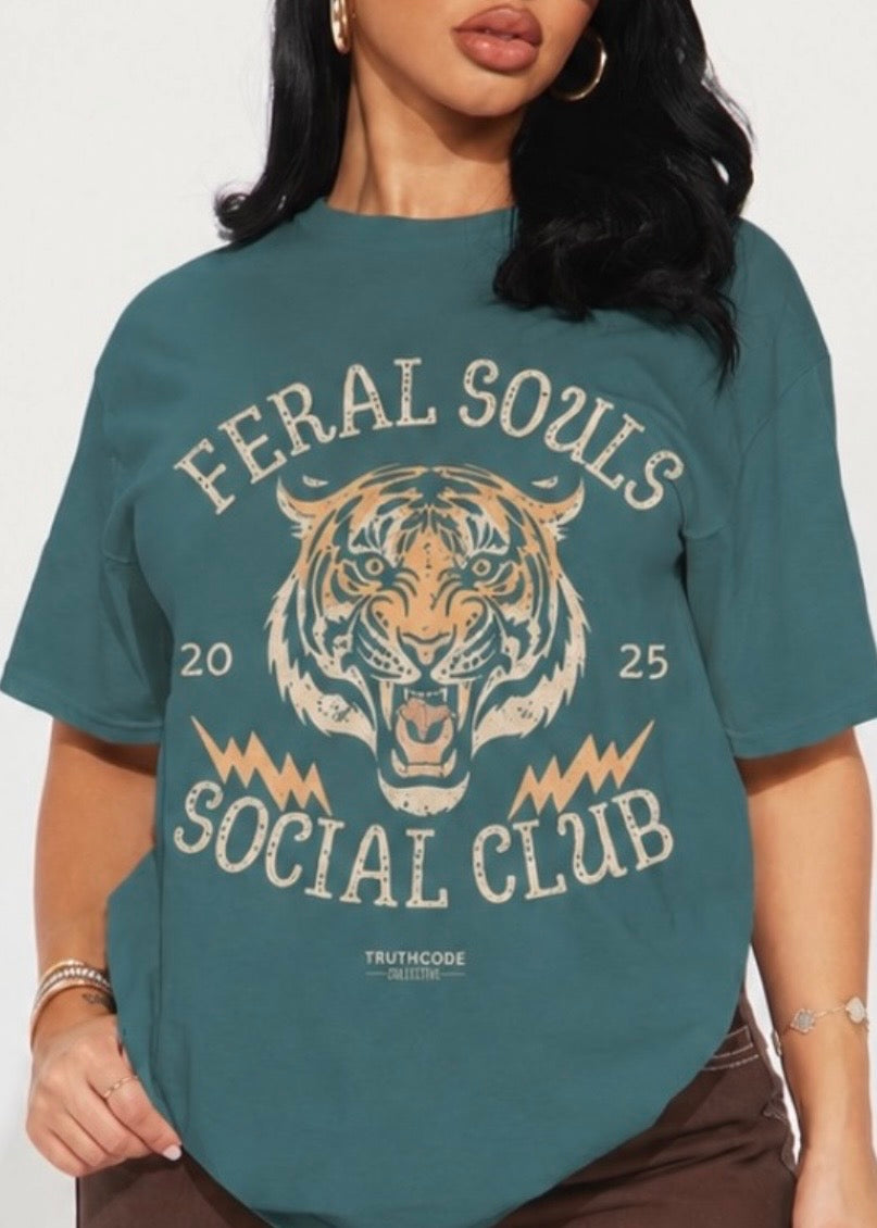 Person wearing a teal t-shirt with a tiger and lightning bolts graphic and text 'Feral Souls Social Club'.