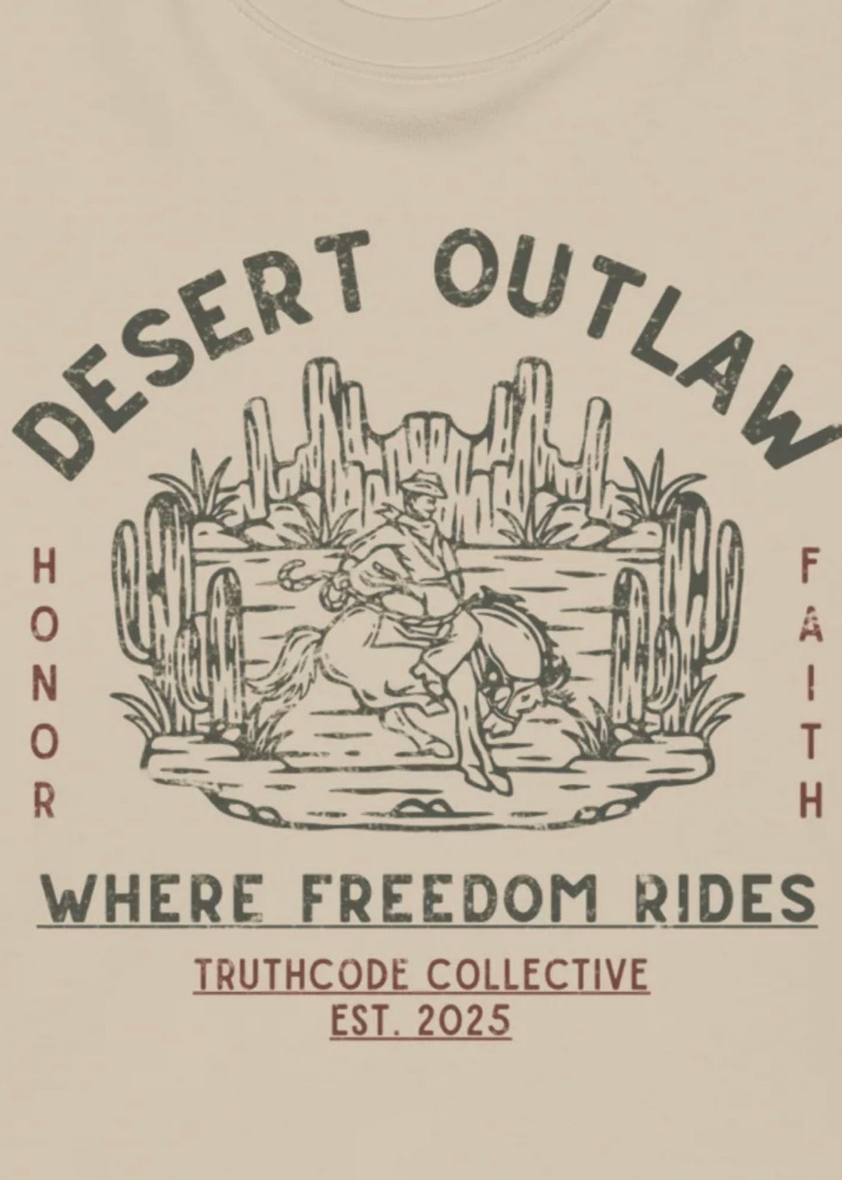Close view of beige t-shirt with text  'Desert Outlaw, where freedom rides' and graphic of cowboy on a bronco in a desert scene
