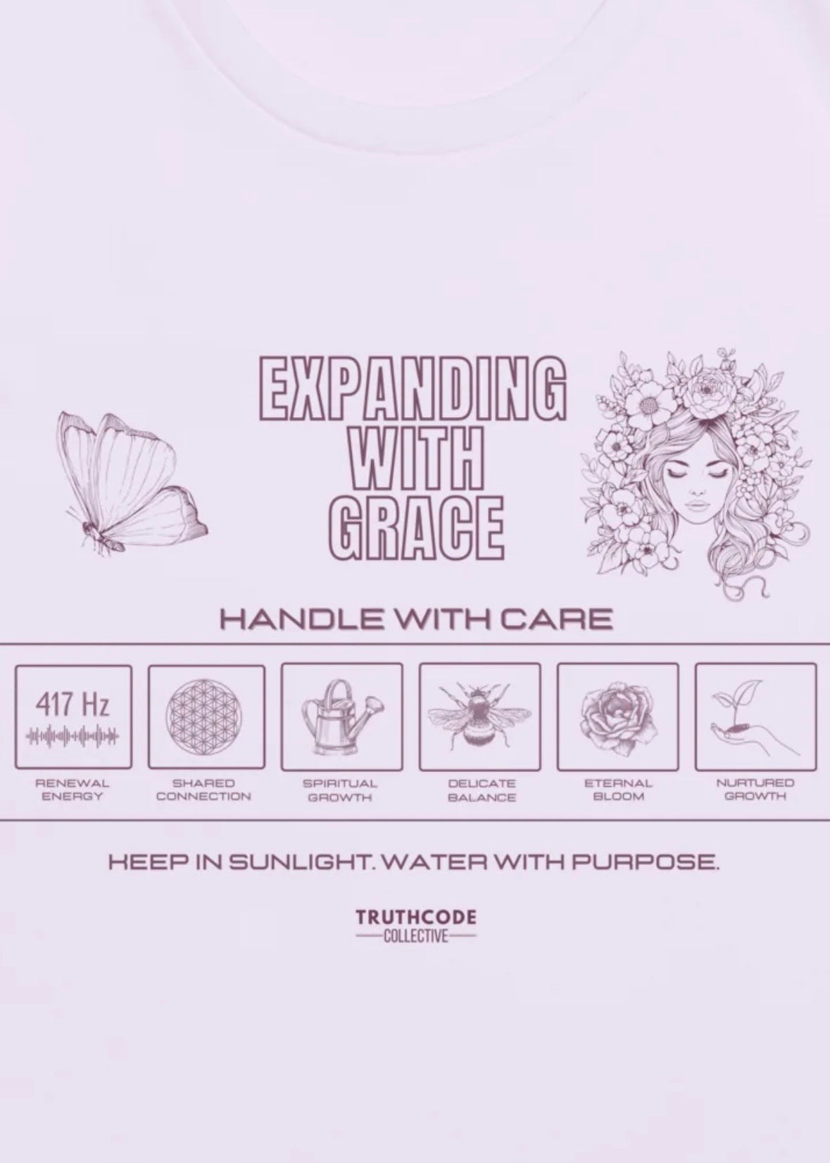 Close view of lavender tee with laundry tag inspired graphic design and text 'Expanding with grace' and symbols relating to expansion