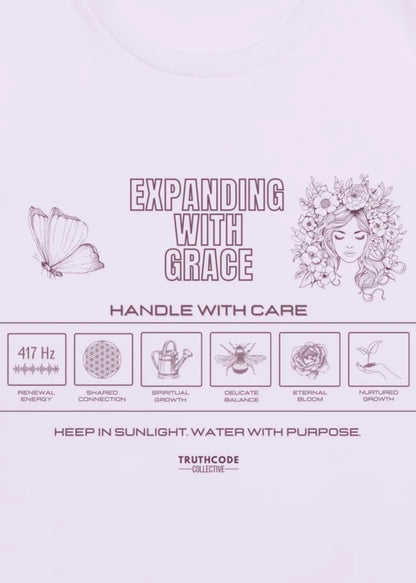 Close view of lavender tee with laundry tag inspired graphic design and text 'Expanding with grace' and symbols relating to expansion