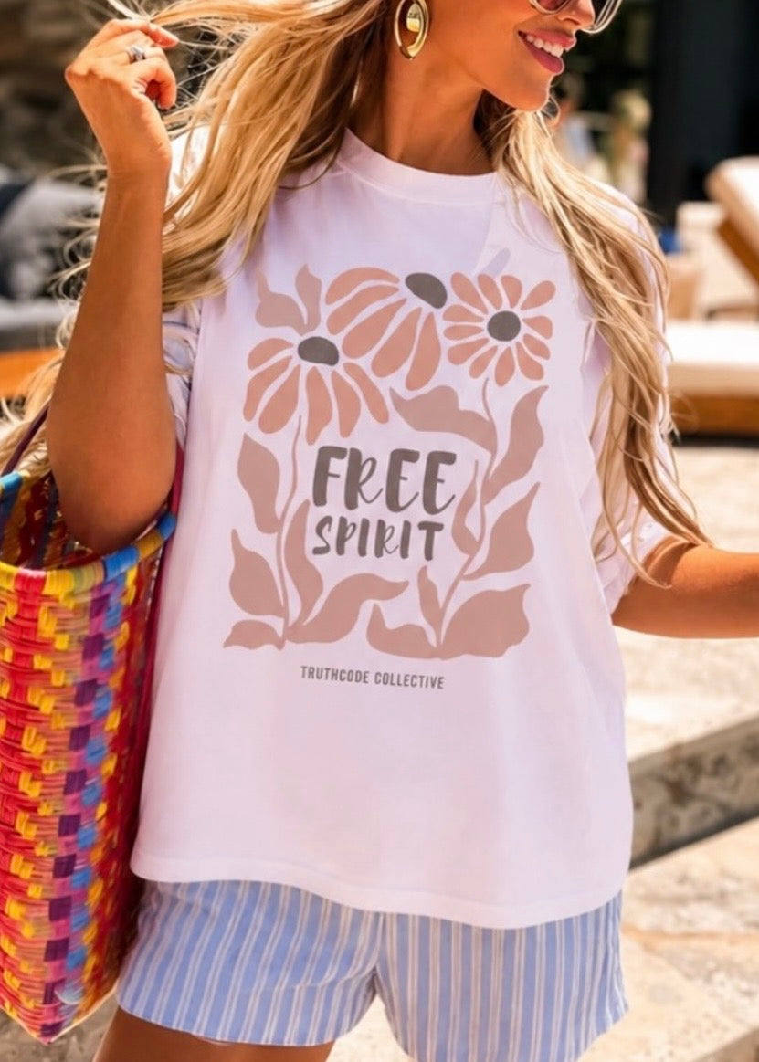 Woman wearing a lavender t-shirt with 'Free Spirit' boho floral design and striped shorts, holding a colorful bag.