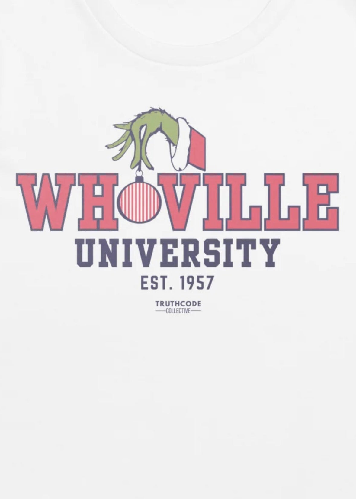 Close view of white t-shirt with text design of 'Whoville University' with a Santa suit style sleeve and green hand holding a Christmas ornament