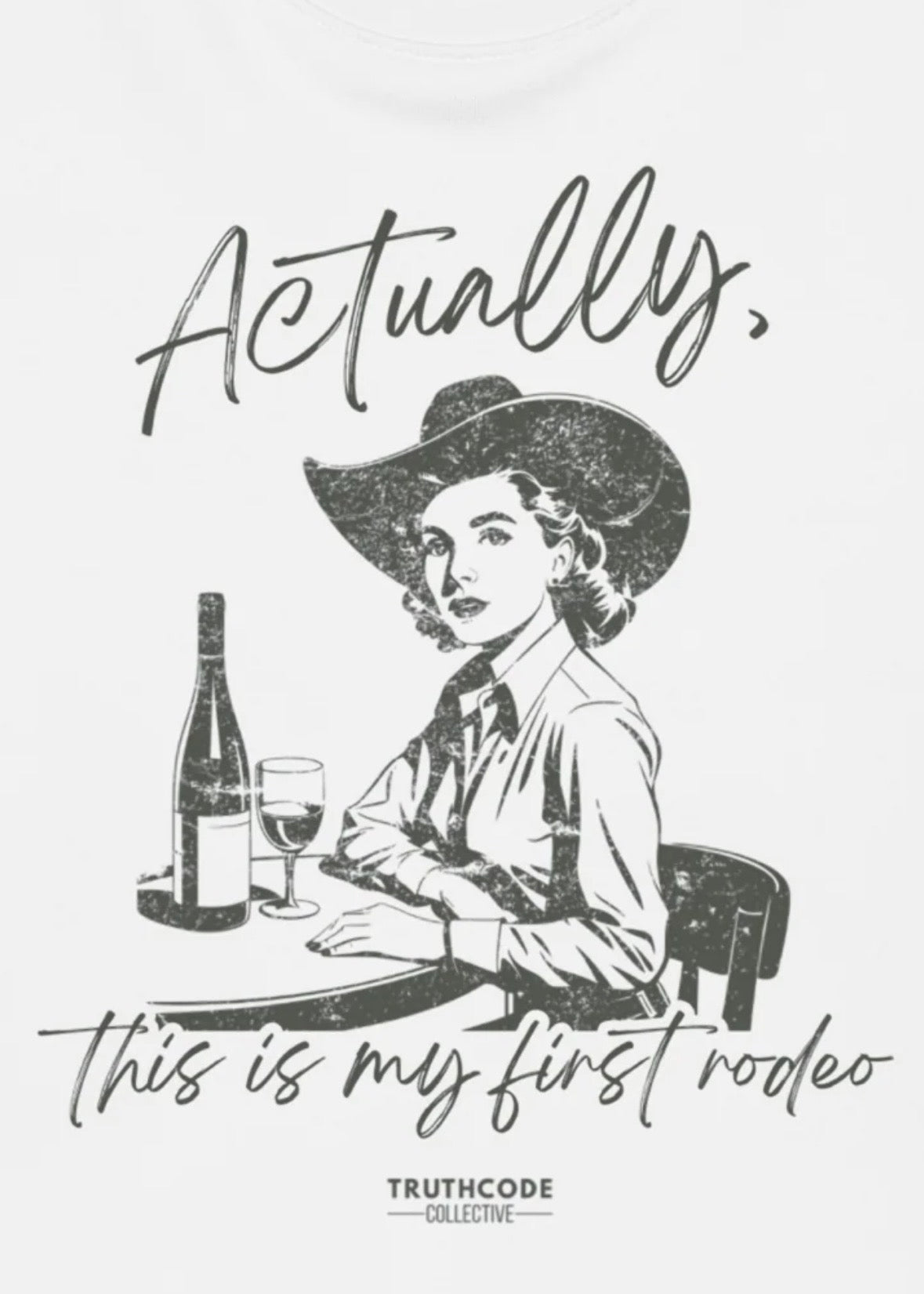 Close view of white t-shirt with vintage style illustration of a woman in a cowboy hat with text 'Actually, this is my first rodeo' and a bottle of wine.