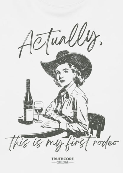 Close view of white t-shirt with vintage style illustration of a woman in a cowboy hat with text 'Actually, this is my first rodeo' and a bottle of wine.