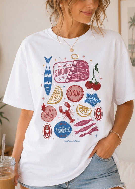 Person wearing a white t-shirt with colorful Mediterranean graphic designs including: sardines, tomatoes, lemons, crab, apple.