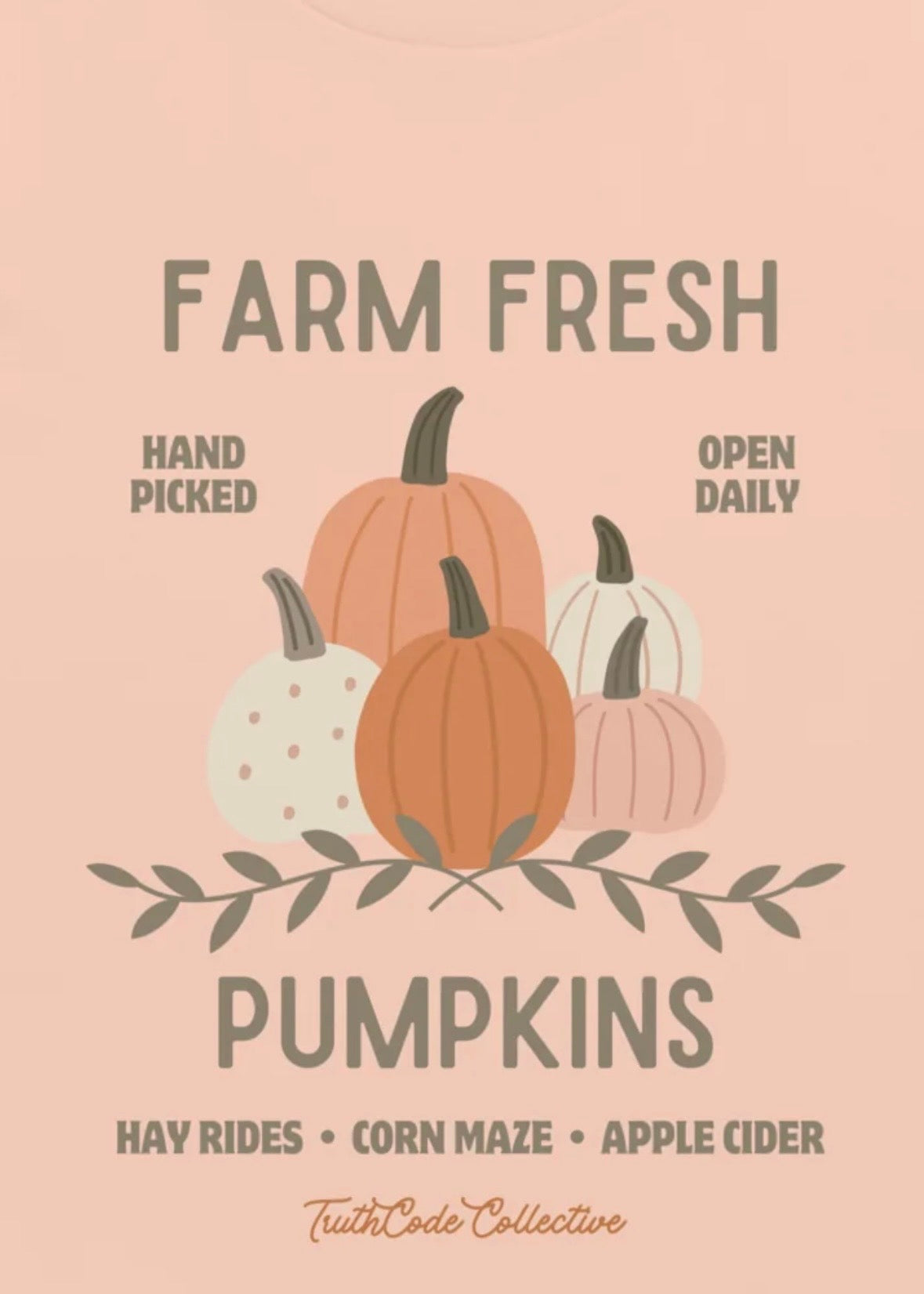 Close view of peach t-shirt  with graphic design of pumpkins and text 'Farm fresh pumpkins, hay rides, corn maze, apple cider' and 'Hand picked, open daily'