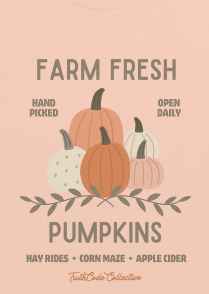 Close view of peach t-shirt  with graphic design of pumpkins and text 'Farm fresh pumpkins, hay rides, corn maze, apple cider' and 'Hand picked, open daily'