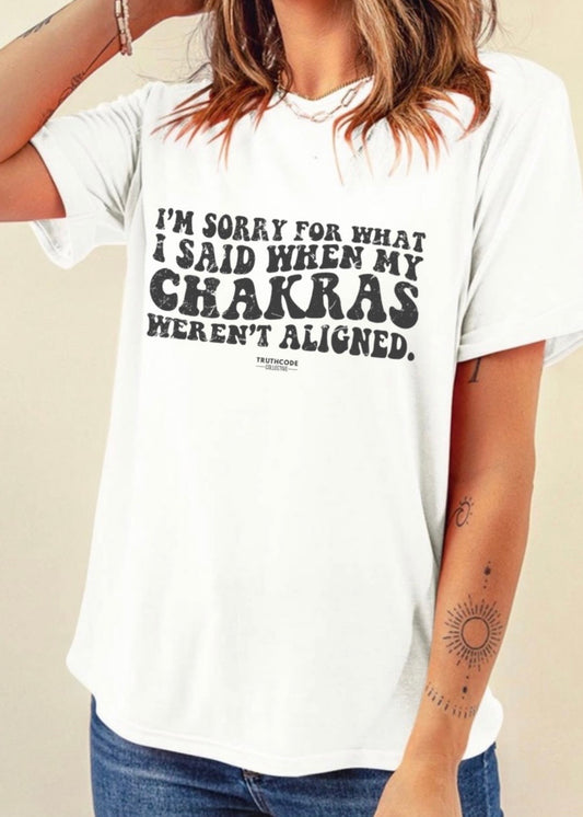 Person wearing a white t-shirt with humorous text 'I'm sorry for what I said when my chakras weren't aligned' design on a plain background