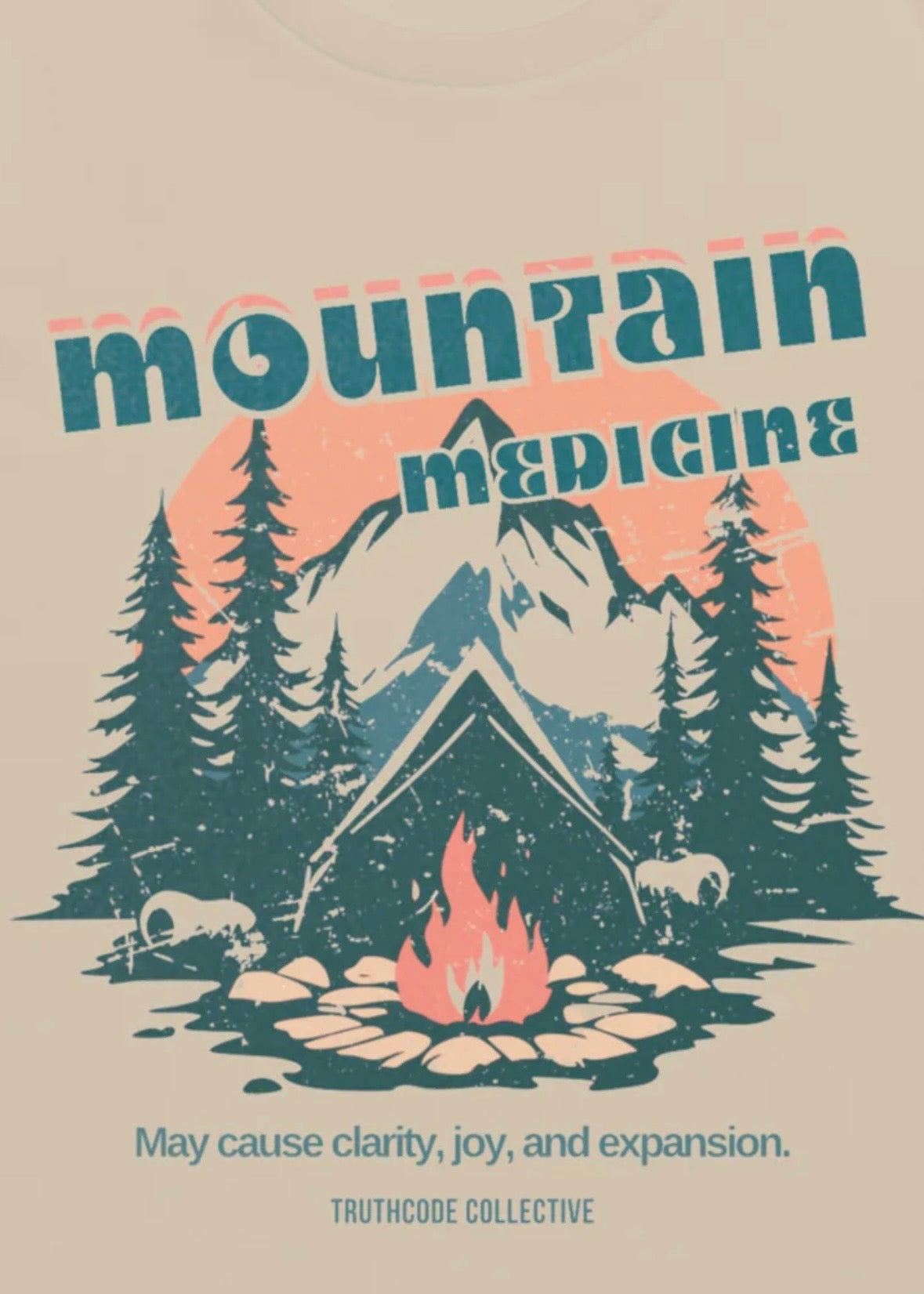 Close view of vintage-style t-shirt design with mountain, cabin, and campfire design, featuring text 'Mountain Medicine' and 'May cause clarity, joy, and expansion.'
