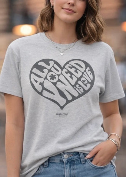 Person wearing a gray t-shirt with a heart-shaped design and text which says ALL YOU NEED IS LOVE.