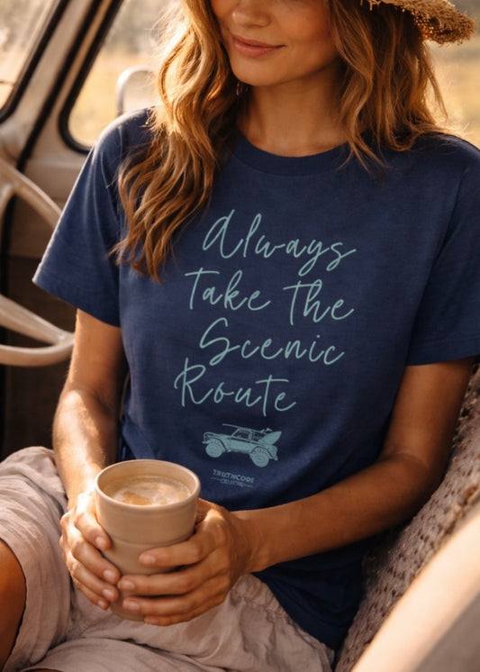 Person wearing a navy blue t-shirt with 'Always Take the Scenic Route' text, holding a cup.