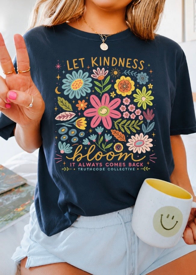 Person wearing a navy t-shirt with floral design and text 'Let Kindness Bloom, It Always Comes Back', holding a mug with a smiley face.