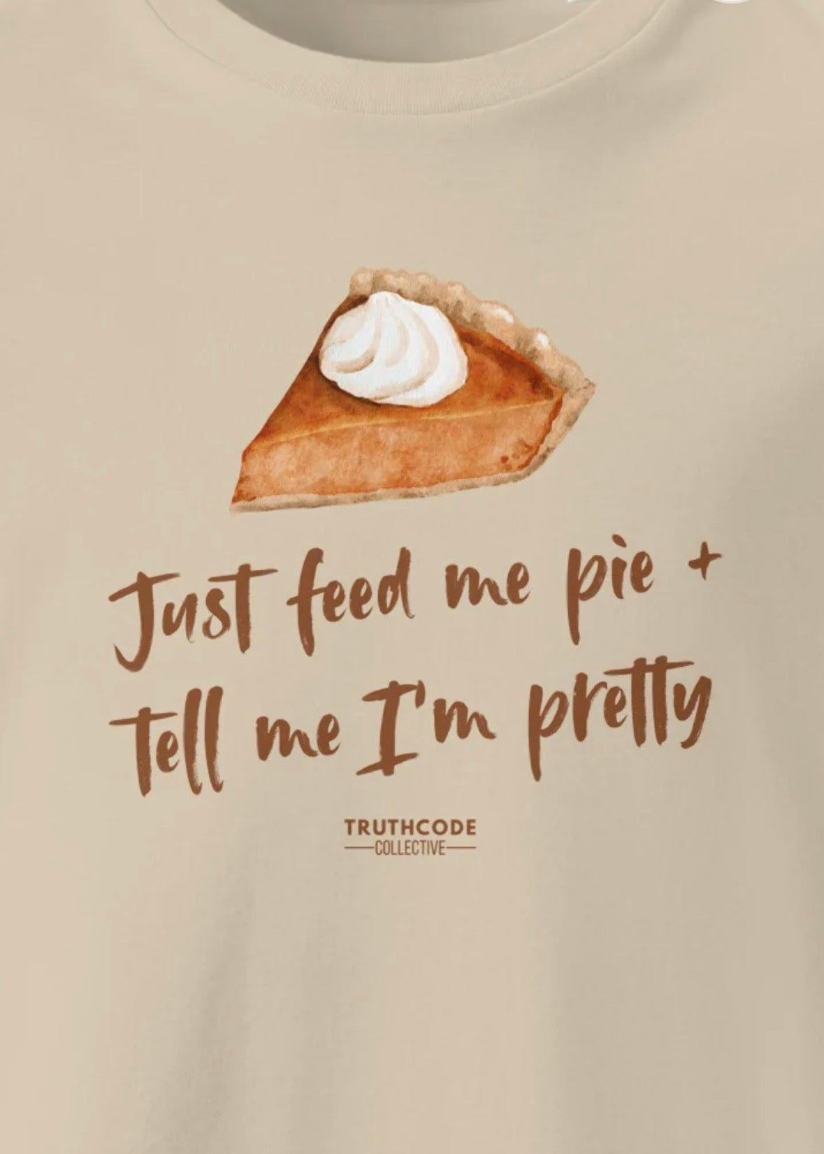 Close view of beige t-shirt with a slice of pie graphic and text 'Just feed me pie + tell me I'm pretty' 