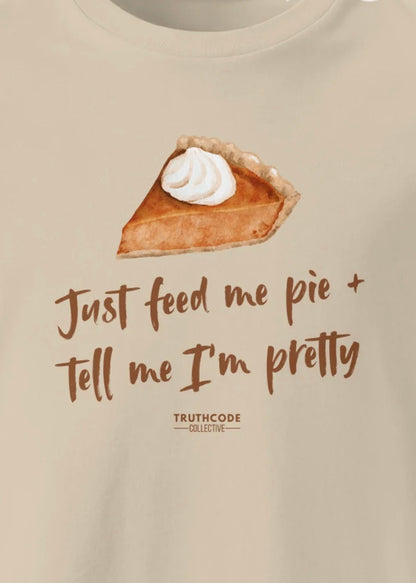 Close view of beige t-shirt with a slice of pie graphic and text 'Just feed me pie + tell me I'm pretty' 
